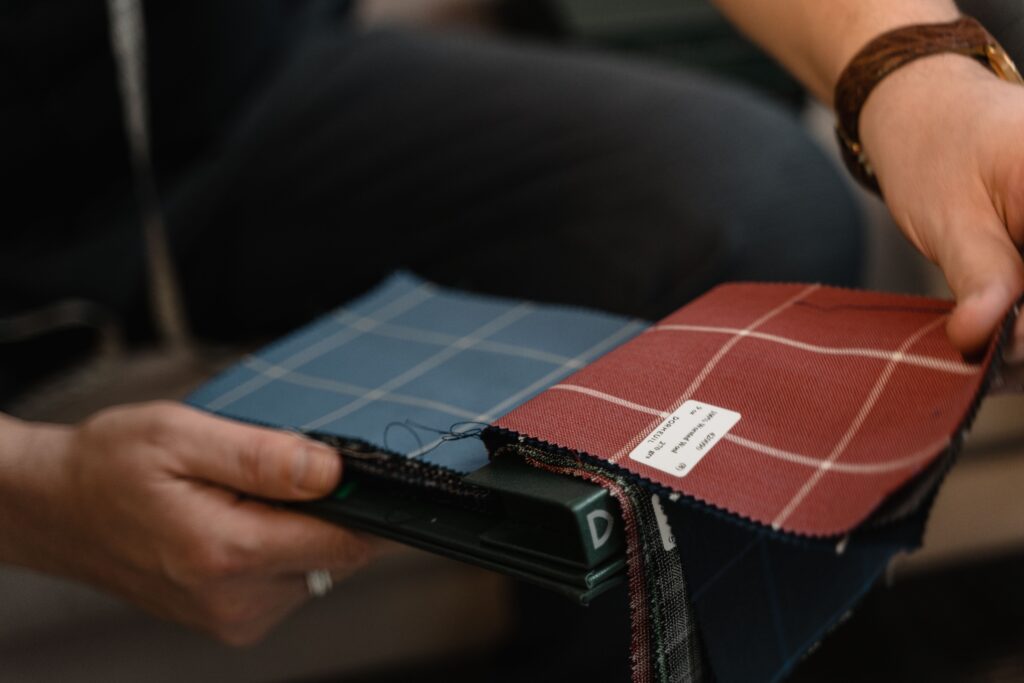 pexels-photo-6766232-6766232 Close-up of hands holding fabric swatches with plaid patterns, ideal for design and textile projects.